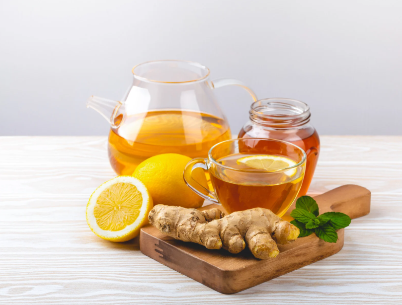 Cup of green tea with fresh ginger and lemon beside it